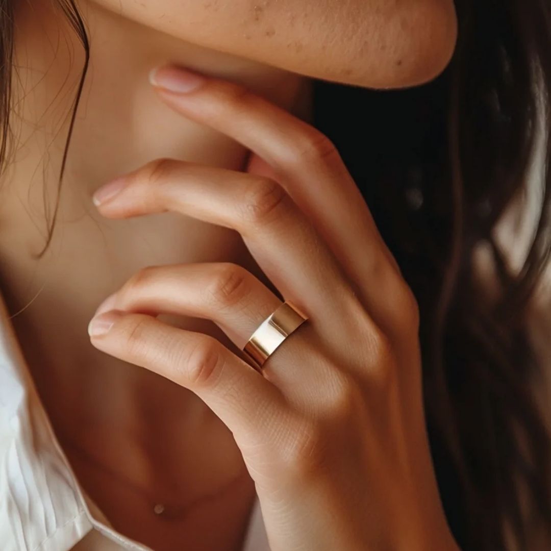 Un primer plano de una mujer de pelo largo castaño con camisa blanca de cuello se toca el cuello, mostrando un Anillo de Magnoterapia - Alivio para la menopausia en su dedo.